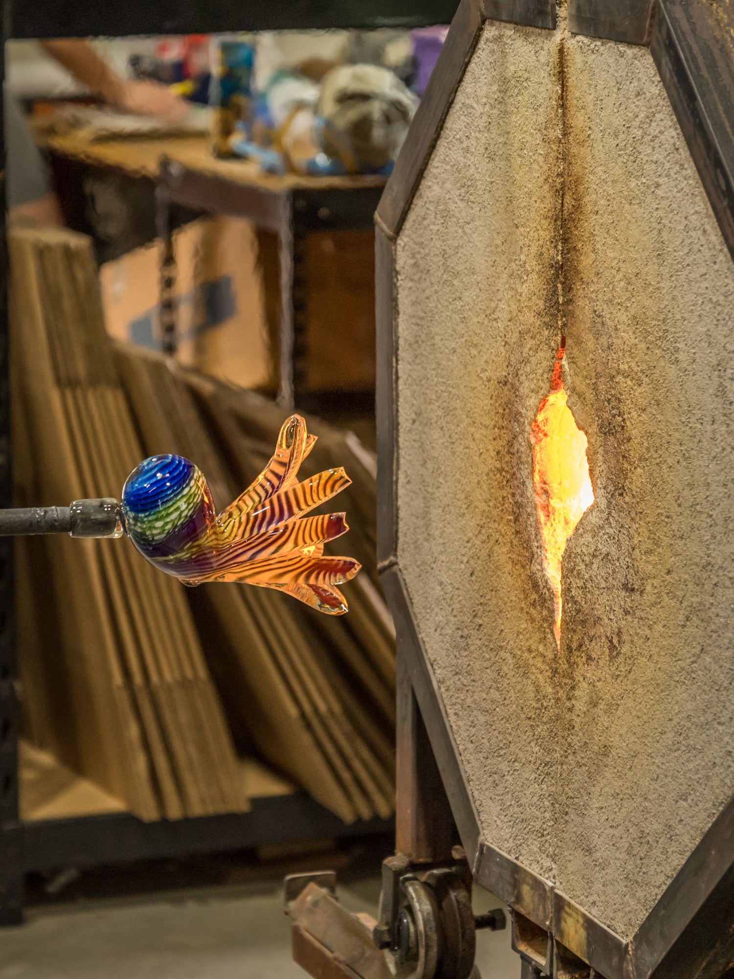 Hopko Art Glass Glassblowing process with a colorful glass piece next to furnace on rod