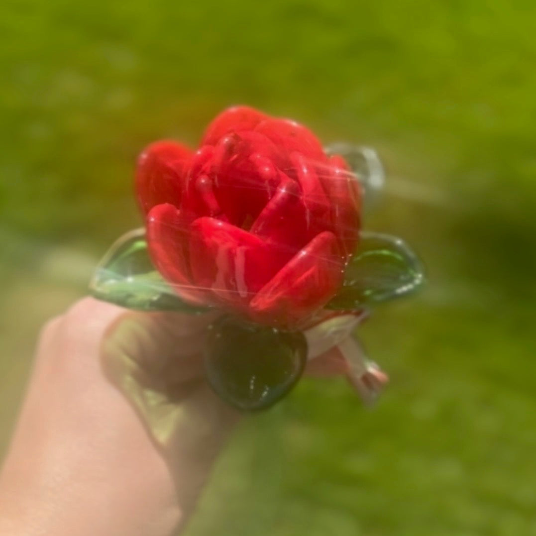Red flower-shaped object held by a hand against a blurred green background