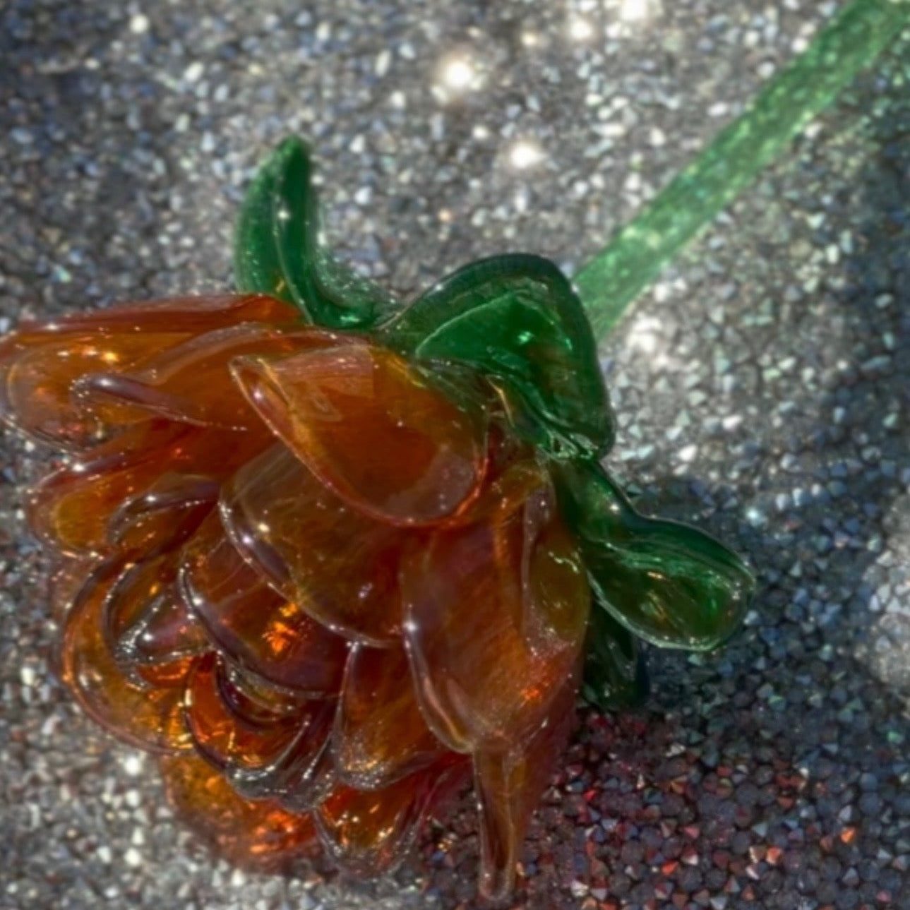 Artificial flower with brown petals and green stem on a glittery surface