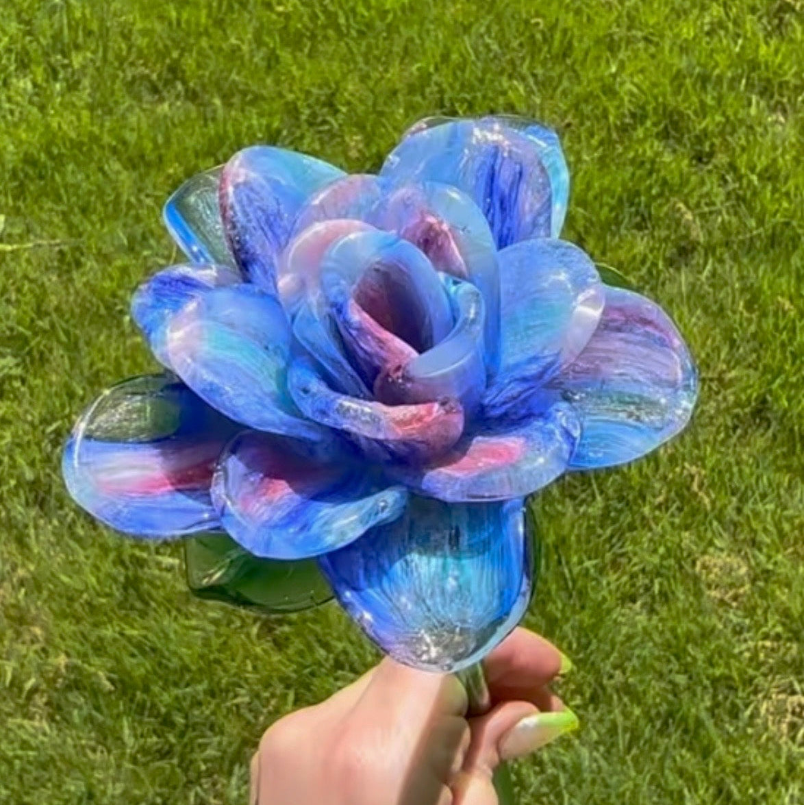 Colorful flower-shaped object held by a hand against a grassy background